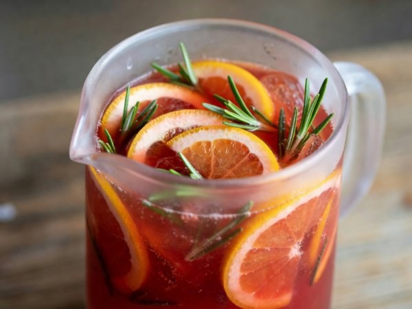 Close-up of a frosted glass pitcher filled with ruby grapefruit and rosemary shrub punch garnished with orange wheels