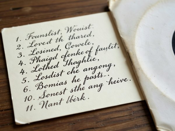 Close-up of a handwritten fountain-pen playlist on a cream index card resting beside a 7-inch vinyl record sleeve