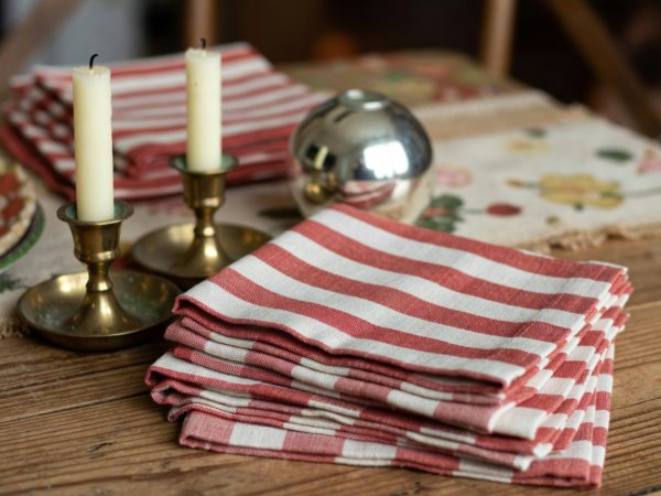 Close-up of striped terracotta linen napkins stacked beside small vintage brass candle holders and a small mirror orb